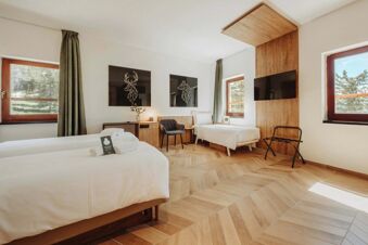 Bright guest room at B&B Hotel Passo Tre Croci Cortina with two single beds, wooden flooring, TV, chair, and windows with curtains
