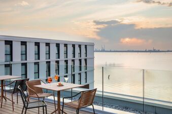 Outdoor seating area with drinks and snacks on table overlooking water and modern building at B&B Hotel Venezia Laguna