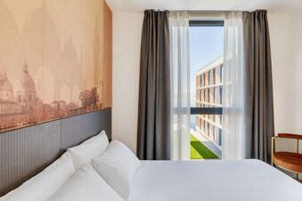 White bed with multiple pillows next to a wall with Venetian mural and window with sheer and dark curtains in B&B Hotel Venezia Laguna