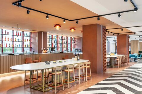 Modern dining area at B&B Hotel Venezia Laguna with a long white table, wooden stools, bar counter, and bottles on shelves