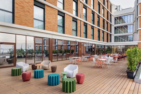 Outdoor patio area with tables, chairs, colorful stools, and plants outside the B&B Hotel Venezia Laguna building