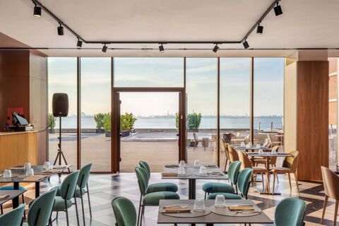 Dining area at B&B Hotel Venezia Laguna with round tables, green and brown chairs, and large glass windows overlooking water and terrace