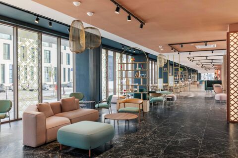 Spacious lounge area with sofas, green chairs, large windows, hanging lights, and decorative shelves at B&B Hotel Venezia Laguna