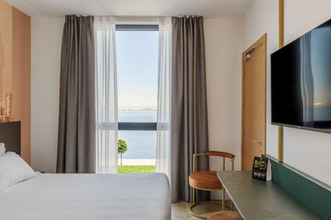 Window with gray curtains and sheer white drapes overlooking water in a room at B&B Hotel Venezia Laguna