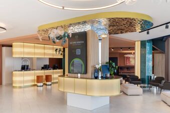 Modern hotel lobby at B&B Hotel Venezia Laguna with a circular illuminated reception desk and digital display board on a wooden stand