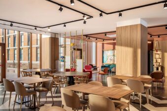 Dining and lounge area in B&B Hotel Venezia Laguna with wooden tables, mixed chairs, large windows, and track lighting