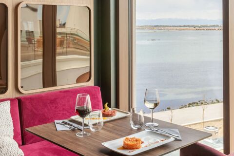 Dining table with two plates of food, glasses of red and white wine, a bright pink bench, and a window view at B&B Hotel Venezia Laguna