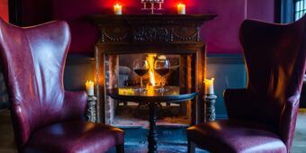 Two red leather chairs with a small black table holding two glasses of red wine in front of a lit fireplace at Hotel du Vin Tunbridge Wells