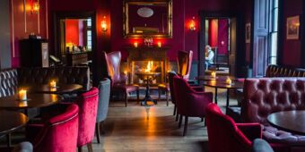 Cozy lounge area with red and gray chairs around tables, a fireplace with candles, and dark wood floors at Hotel du Vin Tunbridge Wells