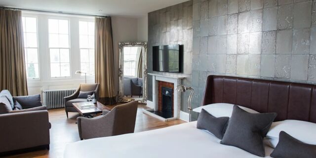 Bright hotel room at Hotel du Vin Tunbridge Wells with a large bed, sofa, armchairs, coffee table, and mounted TV above a fireplace