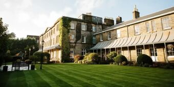 Stone building with multiple windows and chimneys surrounded by green lawns and lamp posts at Hotel du Vin Tunbridge Wells