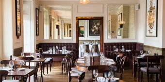 Dining area with wooden tables, chairs, tufted leather benches, mirrors, and wall art in Hotel du Vin Tunbridge Wells