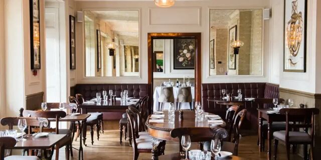 Dining area with wooden tables, chairs, tufted leather benches, mirrors, and wall art in Hotel du Vin Tunbridge Wells