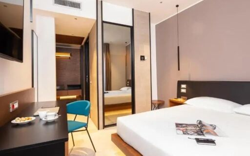 A modern hotel room at The Corner Duomo Hotel with a large bed, black desk, blue chair, and full-length mirror on the wall