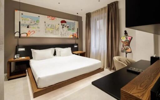 A modern hotel room at The Corner Duomo Hotel with a large bed, bedside tables, abstract wall art, and a mannequin near the window