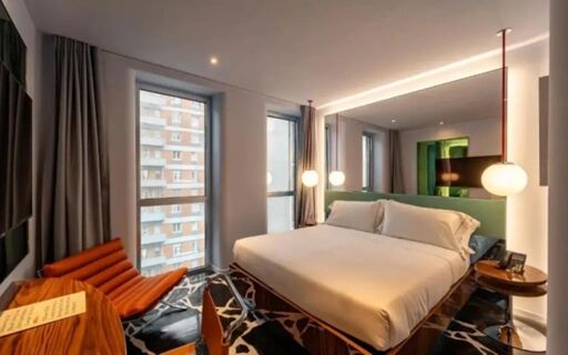 Hotel Calimala room with a large bed, two windows, orange chair, pendant lights, wooden desk, and patterned carpet