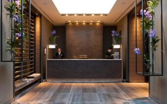 Reception area with two staff members behind a dark wood counter and decorated purple orchids at Starhotels E.c.ho