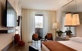 A modern hotel room at Starhotels E.c.ho. with a large bed, two chairs, a TV, and floor-to-ceiling windows with curtains
