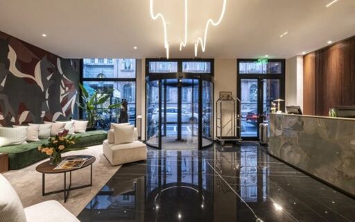 Spacious hotel lobby with black tiled floor, abstract wall art, green sofa, white chairs, and revolving door at Duomo - Hotel Apartments Milano