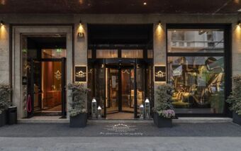 Entrance of Duomo - Hotel Apartments Milano featuring a revolving door, two large glass windows, and decorative plants