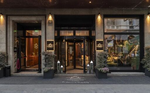 Entrance of Duomo - Hotel Apartments Milano featuring a revolving door, two large glass windows, and decorative plants