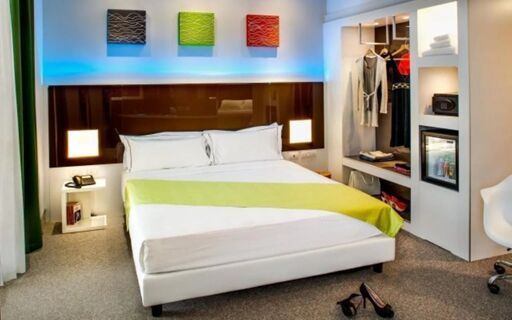 Hotel degli Arcimboldi room with a large bed, green and white bedding, illuminated headboard, open wardrobe, and carpeted floor