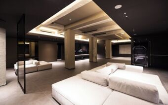 Modern lobby area with white couches, reception desk, luggage cart, and concrete pillars in Joy 124 Milano Hotel