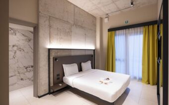 Double bed with white linens and pillows in a room featuring concrete walls and yellow curtains at Joy 124 Milano Hotel