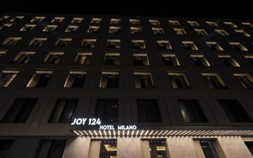 The exterior facade of Joy 124 Milano Hotel at night showing multiple windows and illuminated hotel signage