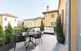 Outdoor terrace seating area with black table, chairs, white cushions, potted plants, and yellow buildings at The Plein Hotel - Small Luxury Hotels of the World