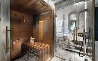 Sauna room with wooden benches and glass door adjacent to a marble bathroom with oval mirror and towel radiator at The Plein Hotel - Small Luxury Hotels of the World