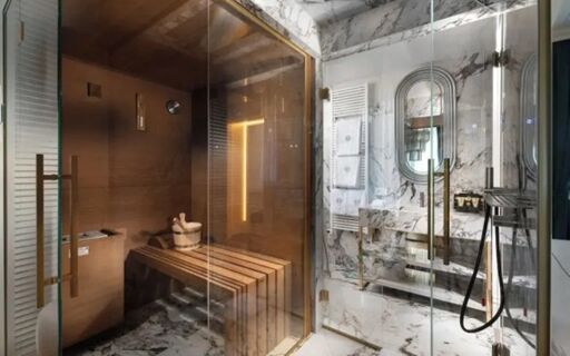 Sauna room with wooden benches and glass door adjacent to a marble bathroom with oval mirror and towel radiator at The Plein Hotel - Small Luxury Hotels of the World