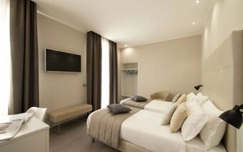 A modern hotel room at Hotel H21 with two single beds, pillows, bedside lamps, TV, bench, and large windows with curtains