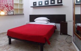 A simple bedroom at Hostel Colours featuring a bed with a red blanket, two stacked pillows, and decorative frames above the headboard