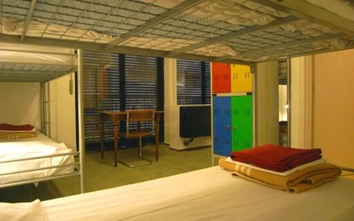 Bunk beds with folded blankets and colorful lockers near a window in a dormitory room at Hostel Colours