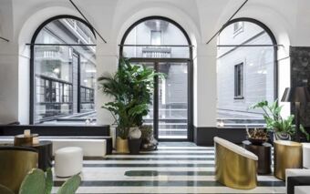 Modern lobby area with large arched windows, green plants, black and gold seating at Senato Hotel Milano