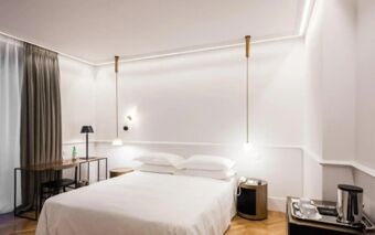 Minimalist hotel room at Senato Hotel Milano with a large bed, bedside tables, hanging lamps, desk, and coffee maker