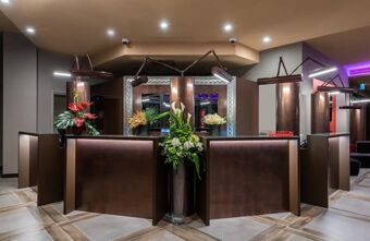 Reception area of Leonardo Royal Hotel Venice Mestre with a brown modern desk, floral arrangements, and overhead lighting