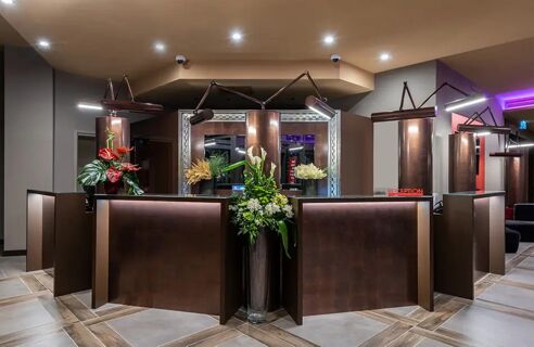 Reception area of Leonardo Royal Hotel Venice Mestre with a brown modern desk, floral arrangements, and overhead lighting