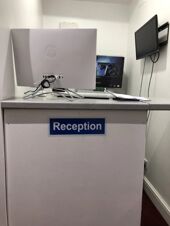 Reception desk with a white HP monitor, papers, and a wall-mounted TV in a room at Leman House