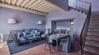 Living and dining area with blue-gray furniture, dining table set, kitchen, and staircase at Podere San Filippo