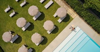 Aerial view of striped lounge chairs with beige umbrellas on grass near a swimming pool at Podere San Filippo hotel