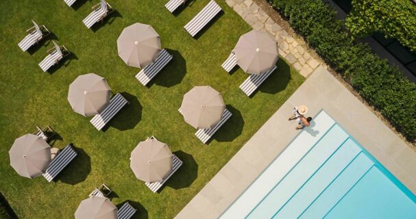 Aerial view of striped lounge chairs with beige umbrellas on grass near a swimming pool at Podere San Filippo hotel