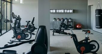 A fitness room at Podere San Filippo featuring exercise bikes, a punching bag, weights, and neatly stacked towels on shelves
