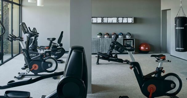 A fitness room at Podere San Filippo featuring exercise bikes, a punching bag, weights, and neatly stacked towels on shelves