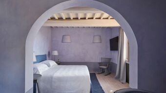 Double bed with white linens and blue headboard in a purple-walled room with a rocking chair and television at Podere San Filippo