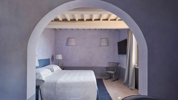 Double bed with white linens and blue headboard in a purple-walled room with a rocking chair and television at Podere San Filippo