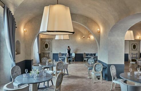 Dining area with round tables, chairs, large hanging lamps, arched ceilings, and a staff member at Podere San Filippo