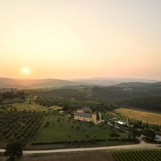 Sunset over rolling hills with olive trees and a large yellow building and pool at Podere San Filippo estate