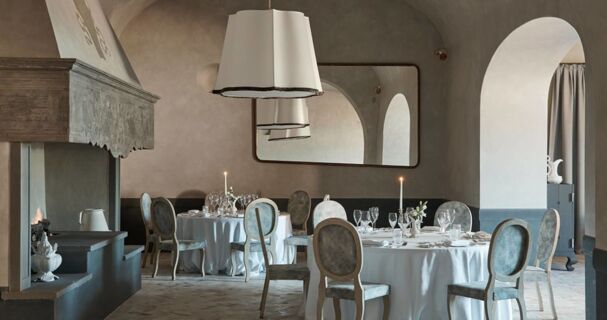 Dining room at Podere San Filippo with round tables set with glassware and candles near a stone fireplace and arched doorway
